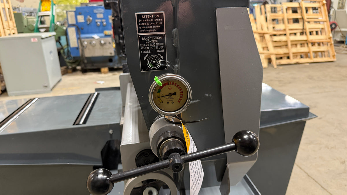 Close-up of a machine with a gauge and control lever, with a blurred background of equipment and wooden pallets.